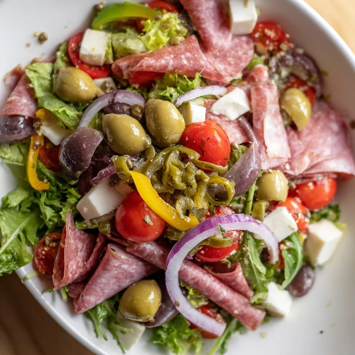 Fresh New Orleans Muffuletta Salad with chopped romaine, salami, provolone, and tangy olive dressing served in a bowl.