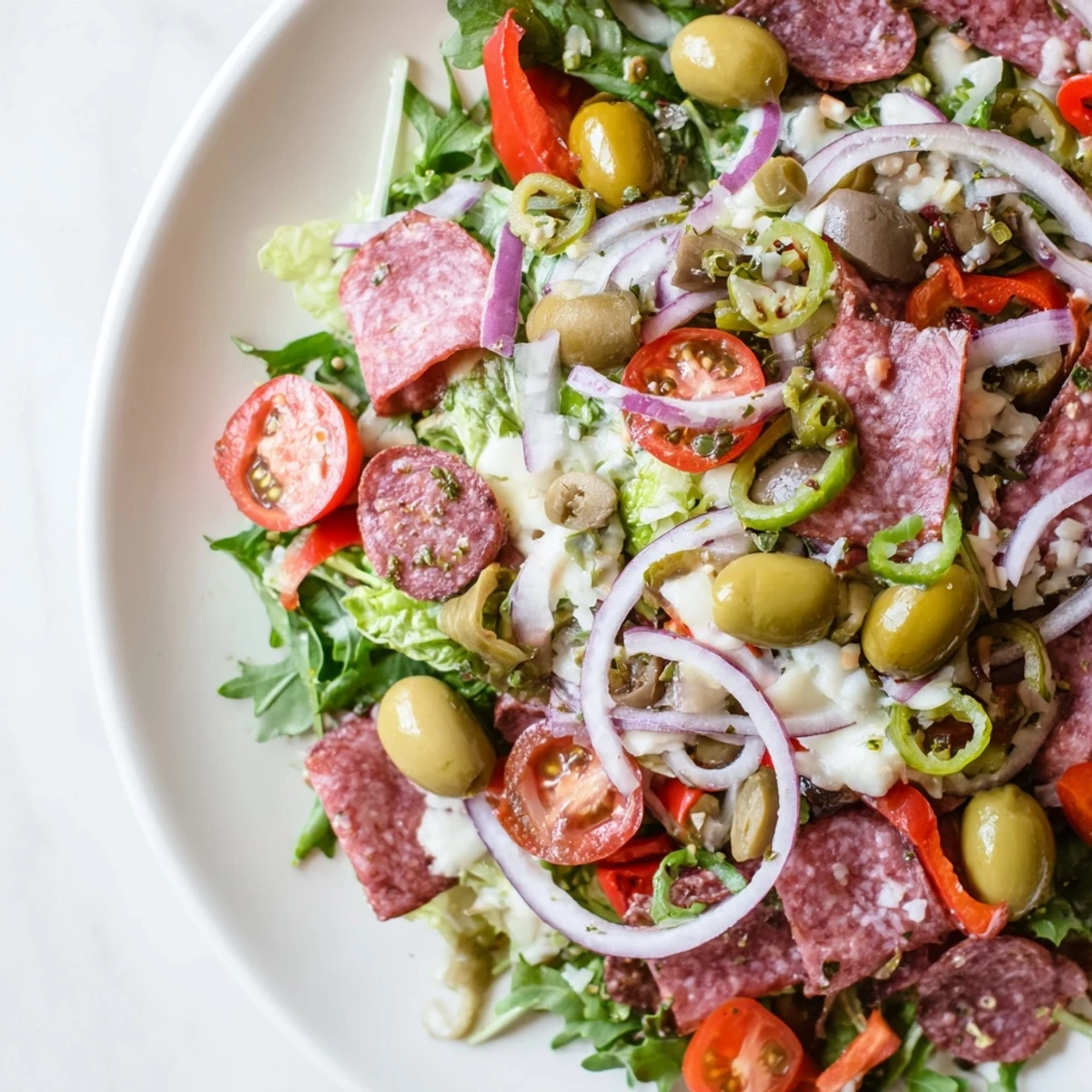 Zesty New Orleans Muffuletta Salad topped with cured meats, melted mozzarella, briny olives, and colorful roasted peppers ready to eat.