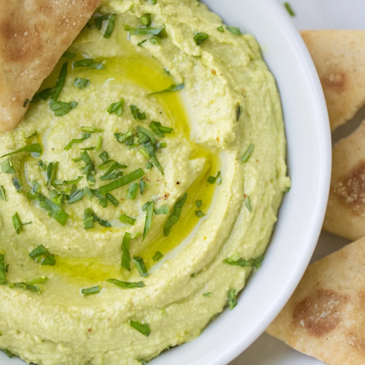 A bowl of green avocado hummus with pita chips, topped with paprika, makes an easy appetizer.