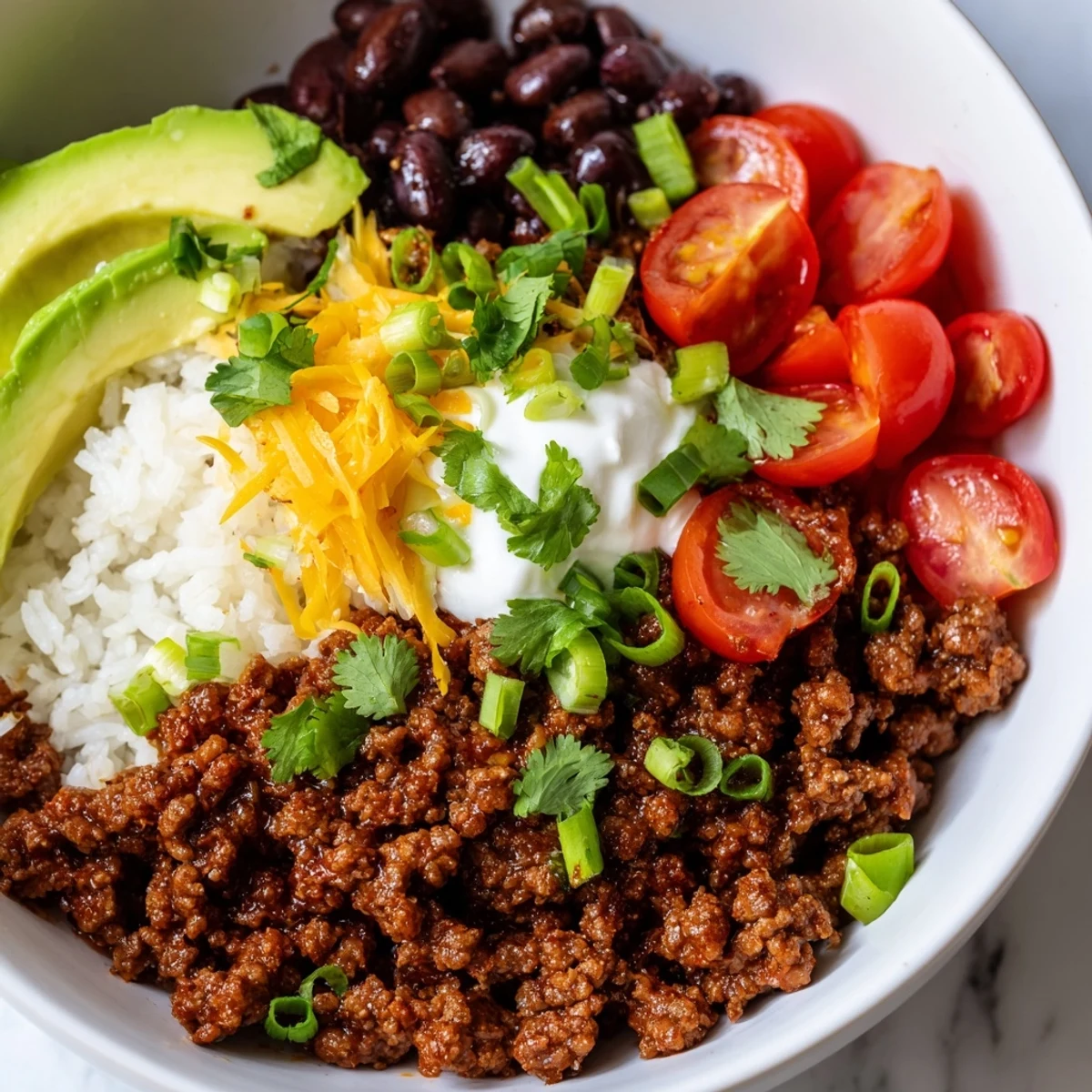 This overhead shot showcases vibrant Beef Burrito Bowls with Rice and Beans, layered with colorful cherry tomatoes, sour cream, and fresh cilantro for a delicious Tex-Mex meal.