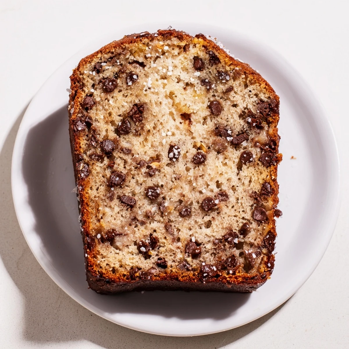 Moist chocolate chip banana bread loaf cooling on a wire rack with ripe bananas nearby.