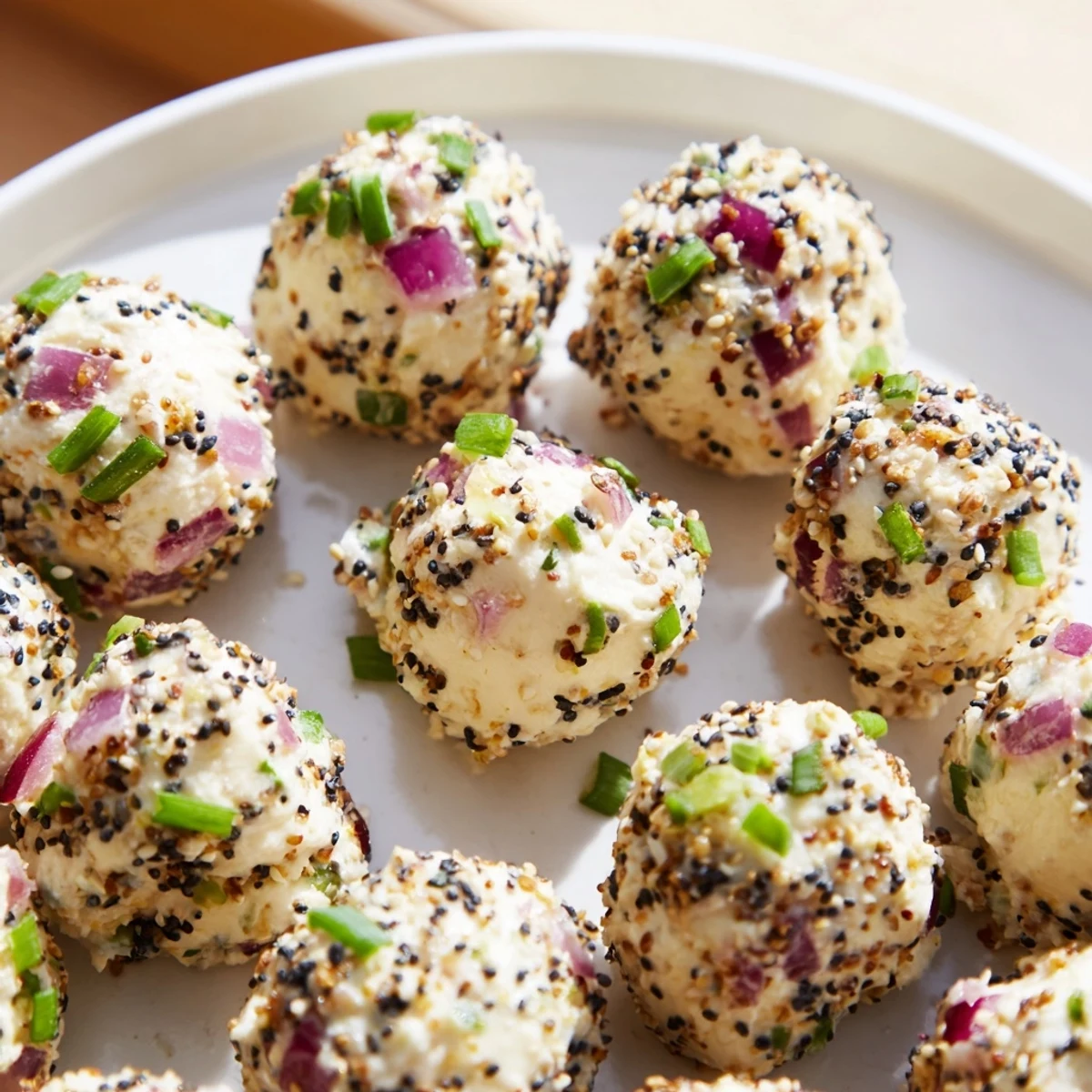 Golden-brown Everything Bagel Cottage Cheese Bites arranged on a white ceramic platter with fresh chives.