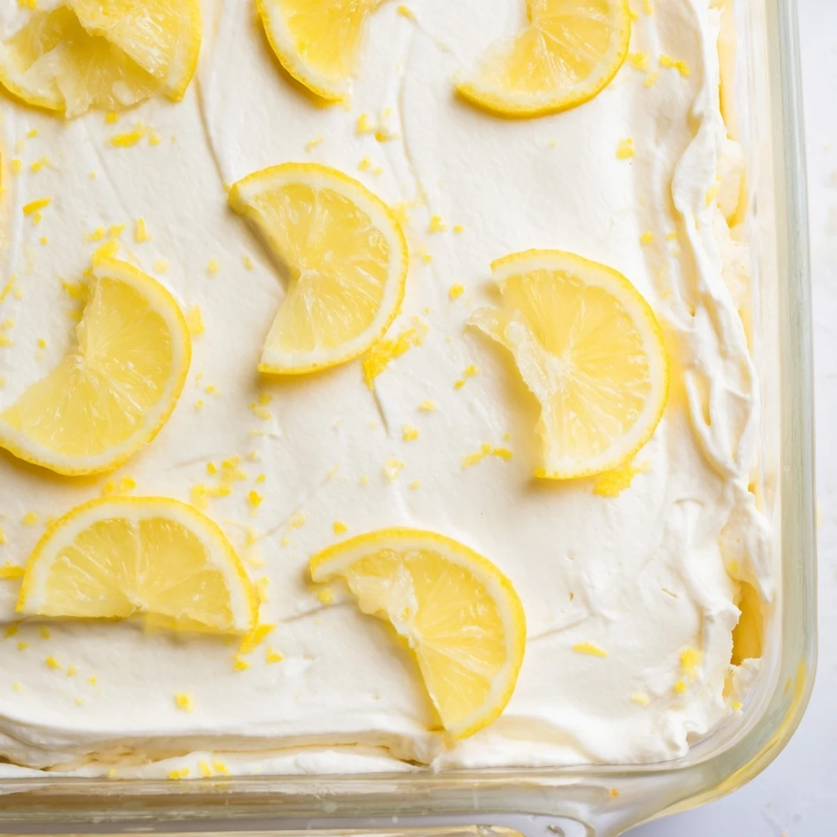 In a white dish, Easy Lemon Tiramisu No Bake Dessert is garnished with fresh lemon slices and bright zest.