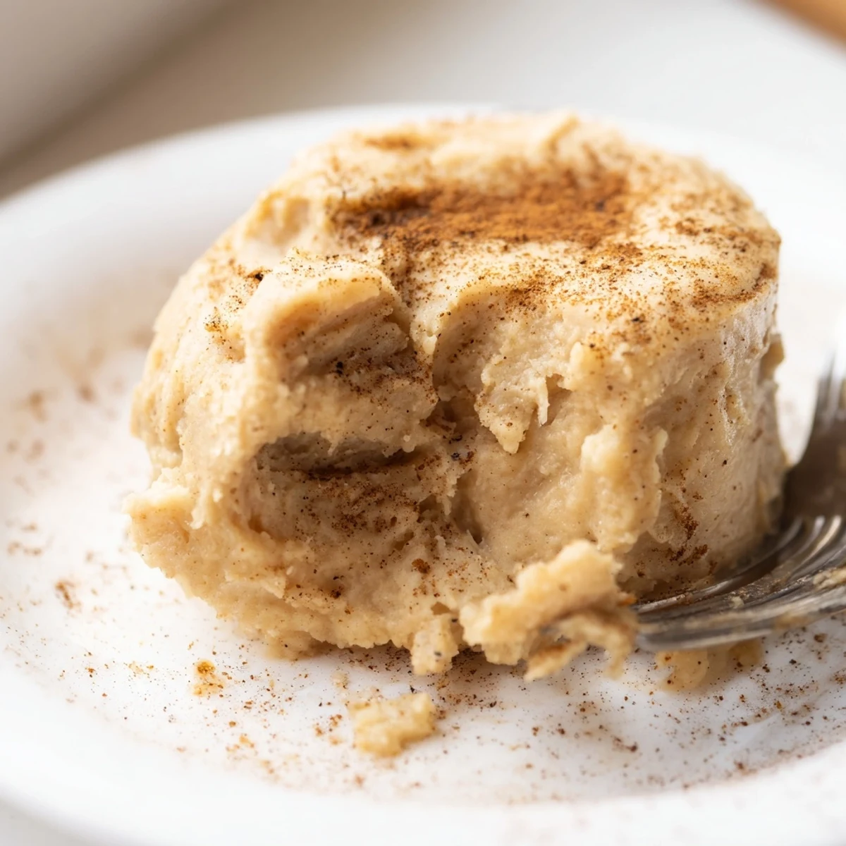 A warm slice of Baked Pumpkin Spice Pudding, topped with whipped cream and a dusting of cinnamon, served in a ceramic dish.