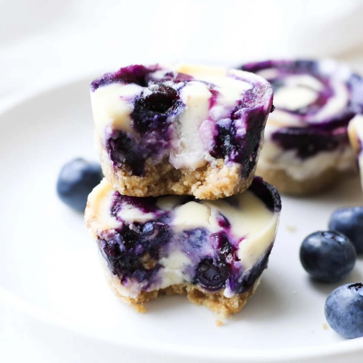 Frosted Blueberry Cheesecake Protein Bites rest on a marble board, showing creamy centers and vibrant berry swirls for a healthy snack.