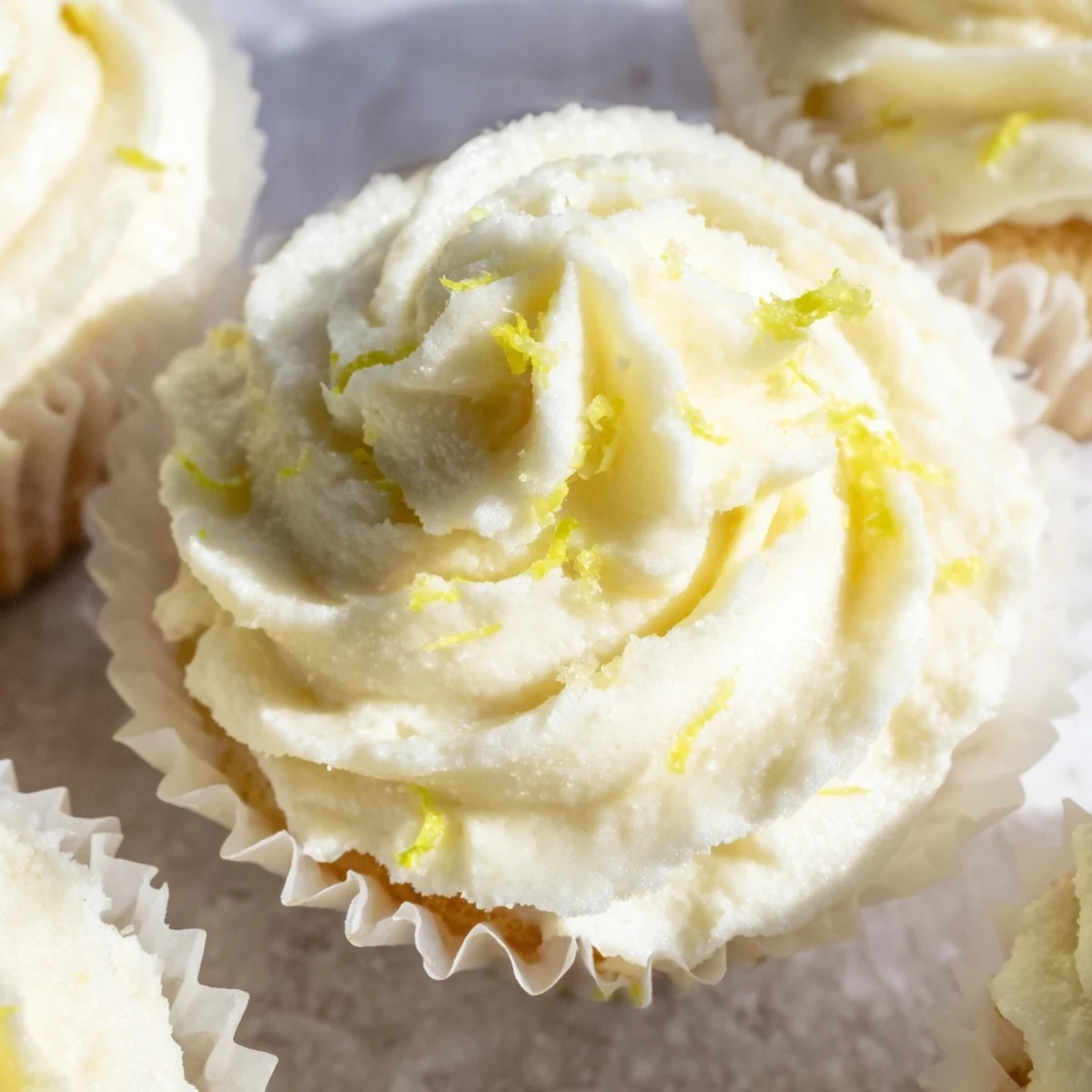 Freshly frosted Elderflower Cupcakes arranged on a rustic plate with a garnish of lemon zest.