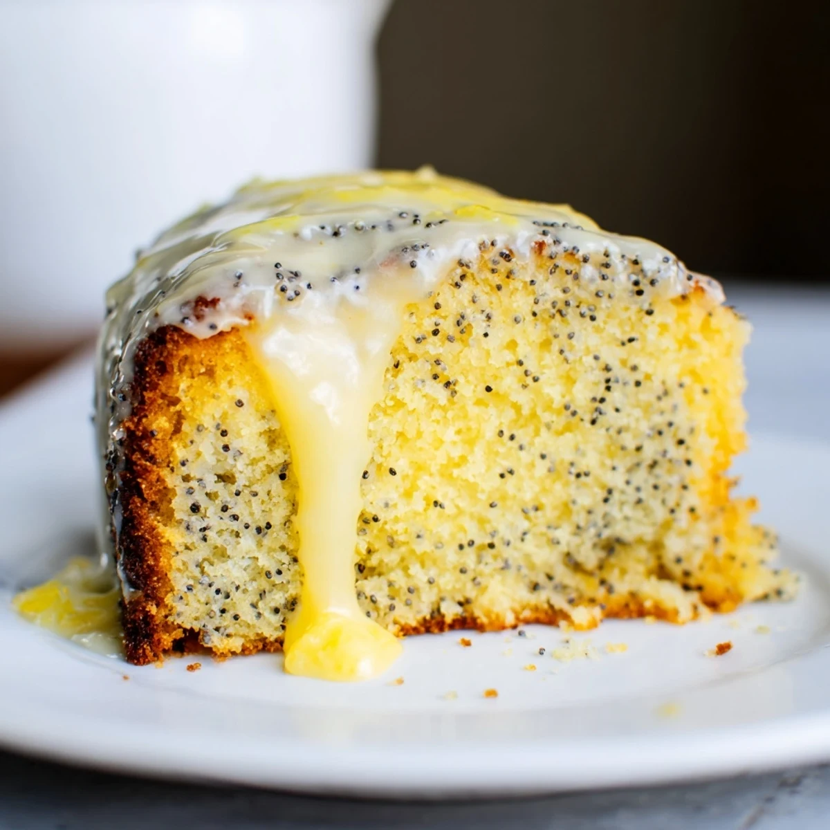 Golden-brown Lemon Poppy Seed Cake with a glossy lemon glaze on a white plate, perfect for afternoon tea.