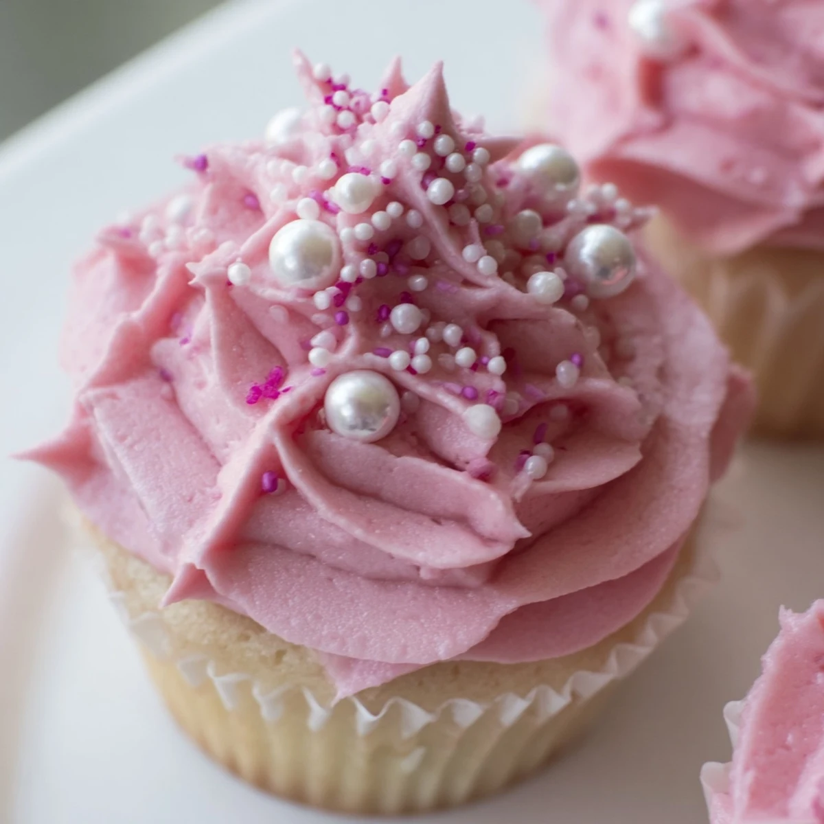A close-up of Girl Baby Shower Cupcakes with fluffy pink buttercream swirls, decorated with tiny edible pearls on a pastel cupcake liner.