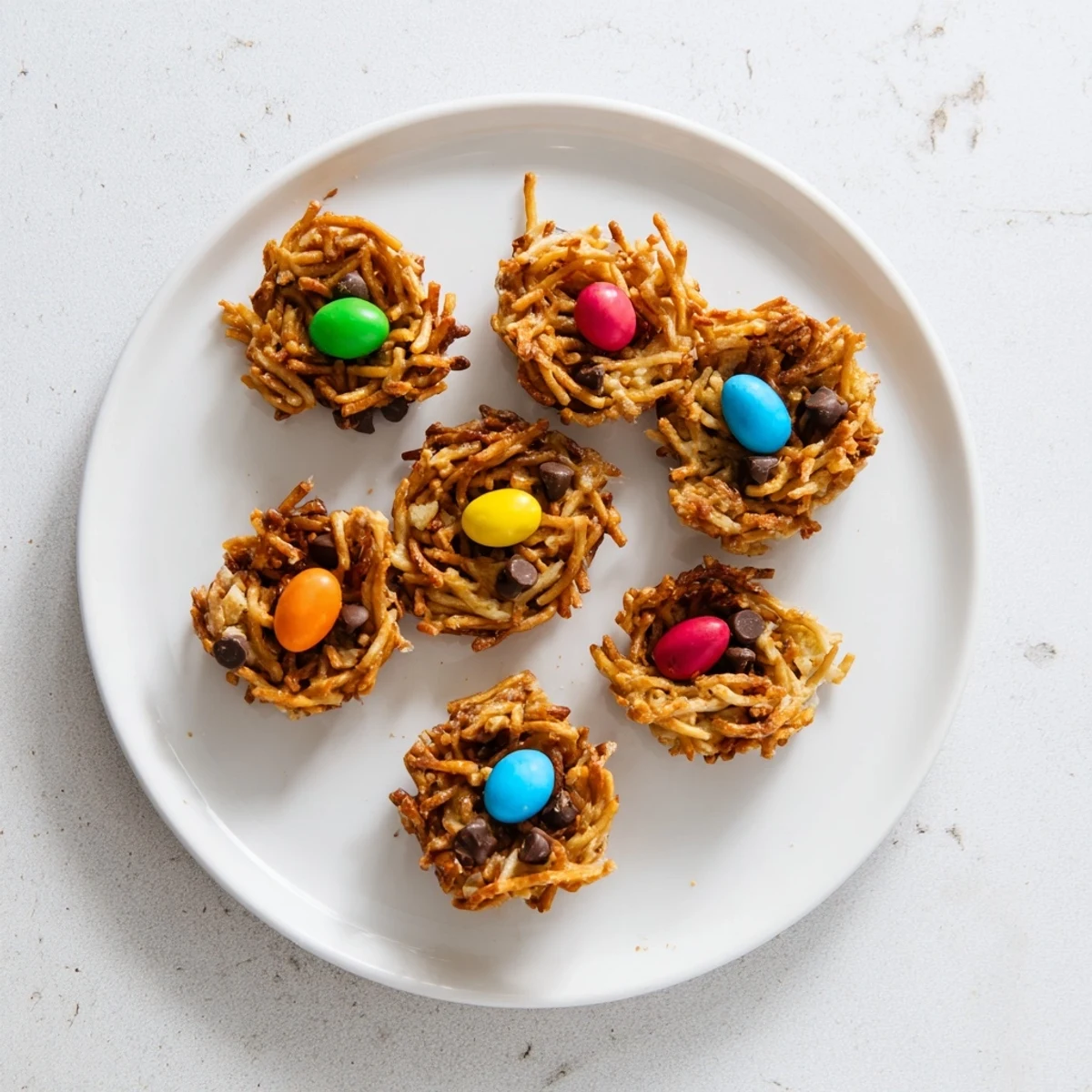 Platter of no-bake Easter Birds Nest Cookies with Peanut Butter and Chocolate served on a marble countertop with scattered candy eggs.