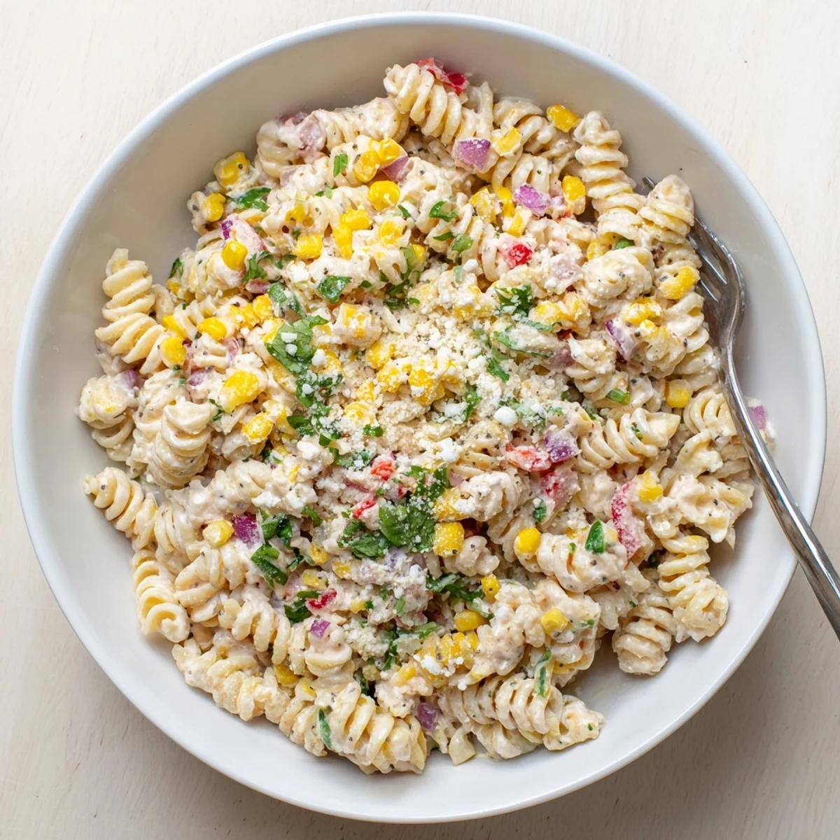 Colorful bowl of Mexican street corn pasta salad featuring rotini tossed with zesty vegetables and tangy cheese garnish
