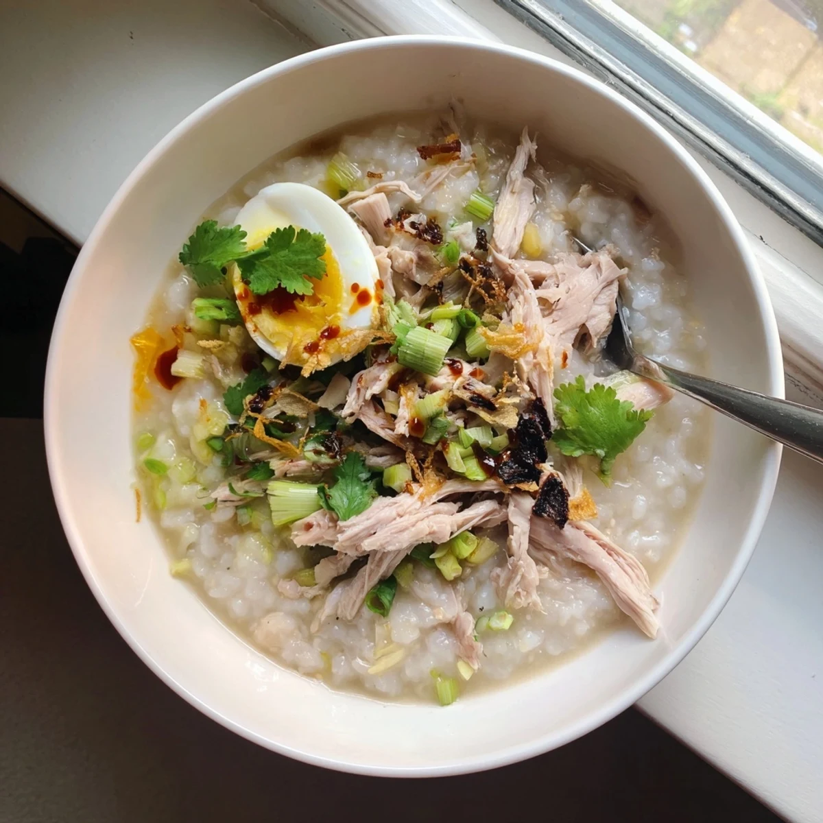 Savory leftover Thanksgiving turkey congee porridge with shredded meat, green onions, and sesame oil on a wooden spoon