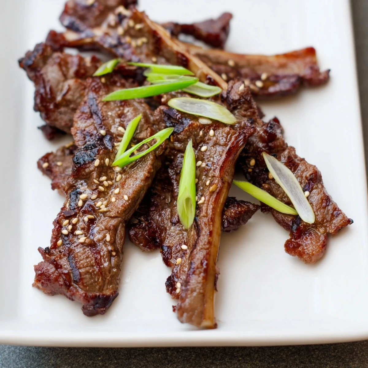 Charred Korean Galbi grilled ribs glazed with caramelized soy and sesame marinade on a white platter