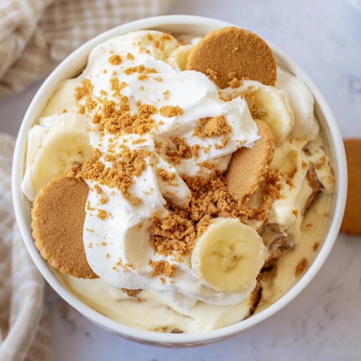 Glass trifle dish revealing layered Biscoff banana pudding with fresh banana slices and whipped cream topping