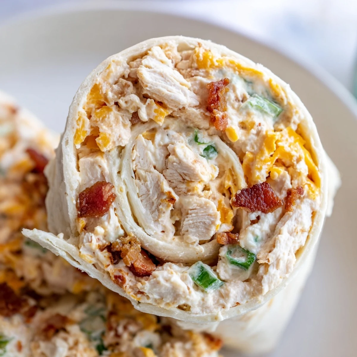 Tightly rolled tortilla wraps filled with seasoned crack chicken ready for chilling and slicing