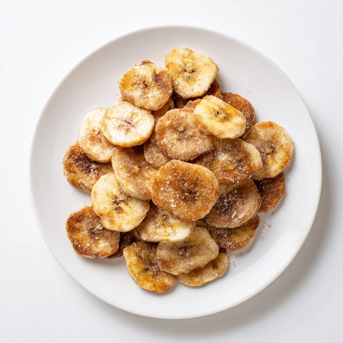 Golden brown cinnamon sugar air fryer banana chips arranged on a white serving plate
