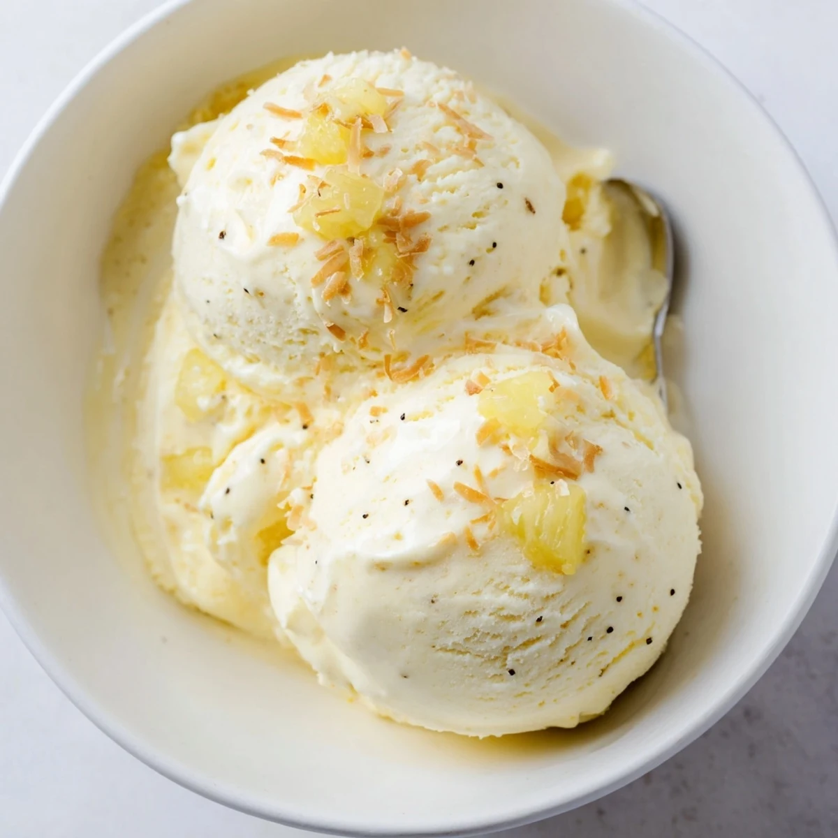 Glass dish of Creamy Pineapple Ice Cream, silky texture, lemon zest garnish