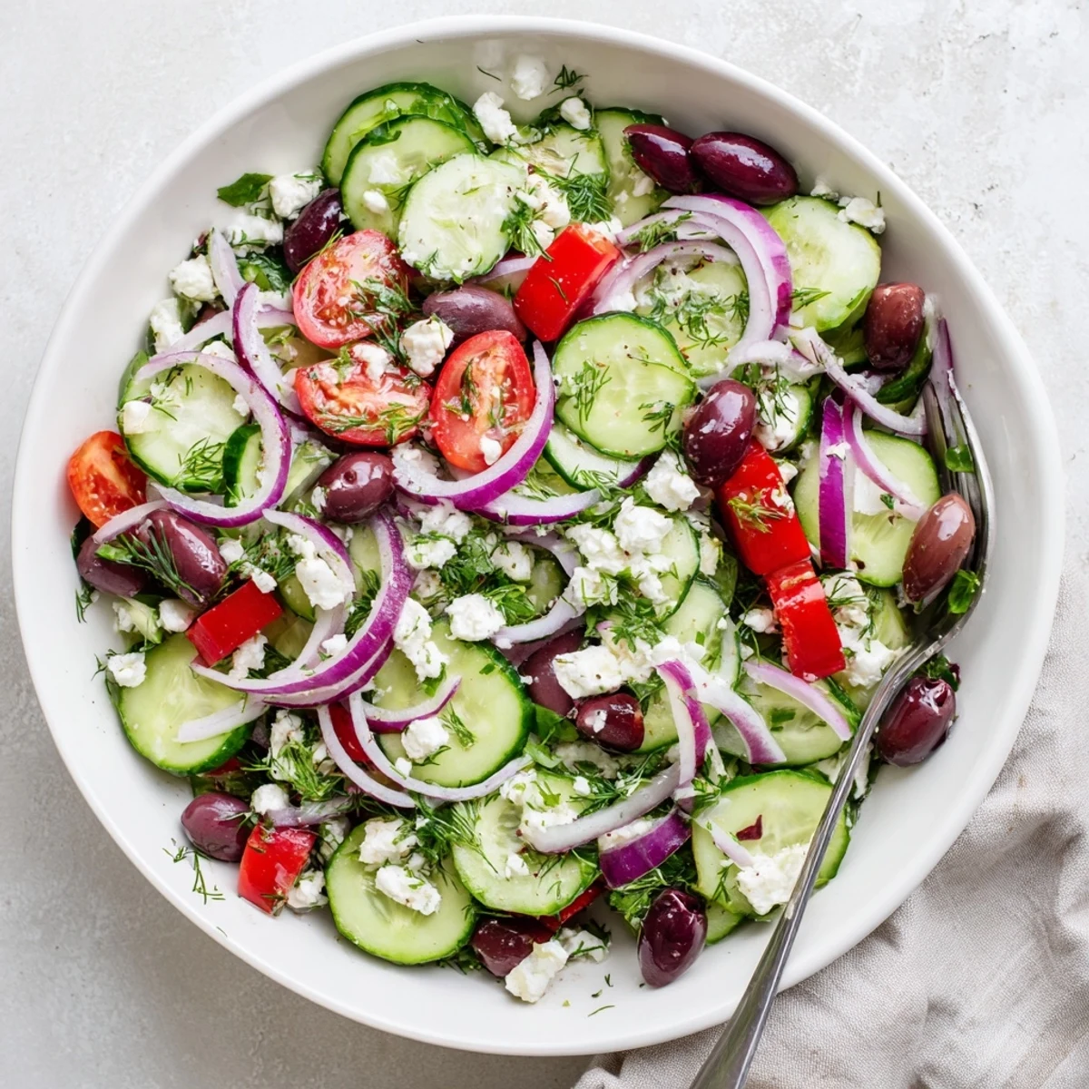 Colorful Mediterranean cucumber salad topped with crumbled feta and fresh herbs on a white plate