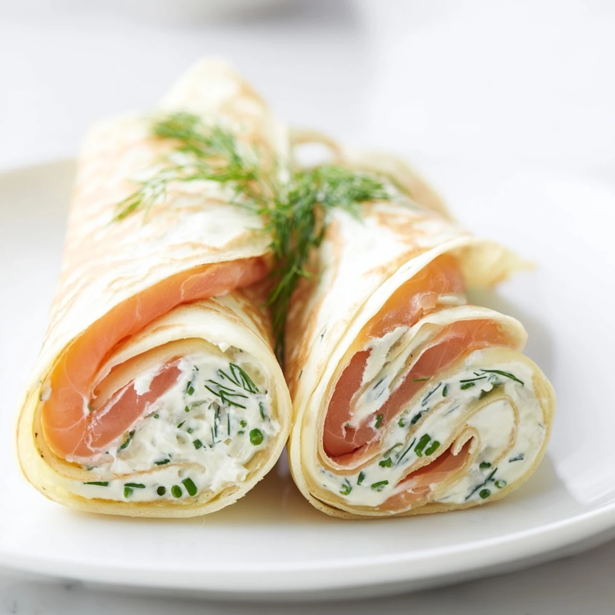 Delicate French crepes wrapped around silky smoked salmon and herb cream cheese on a white serving platter.