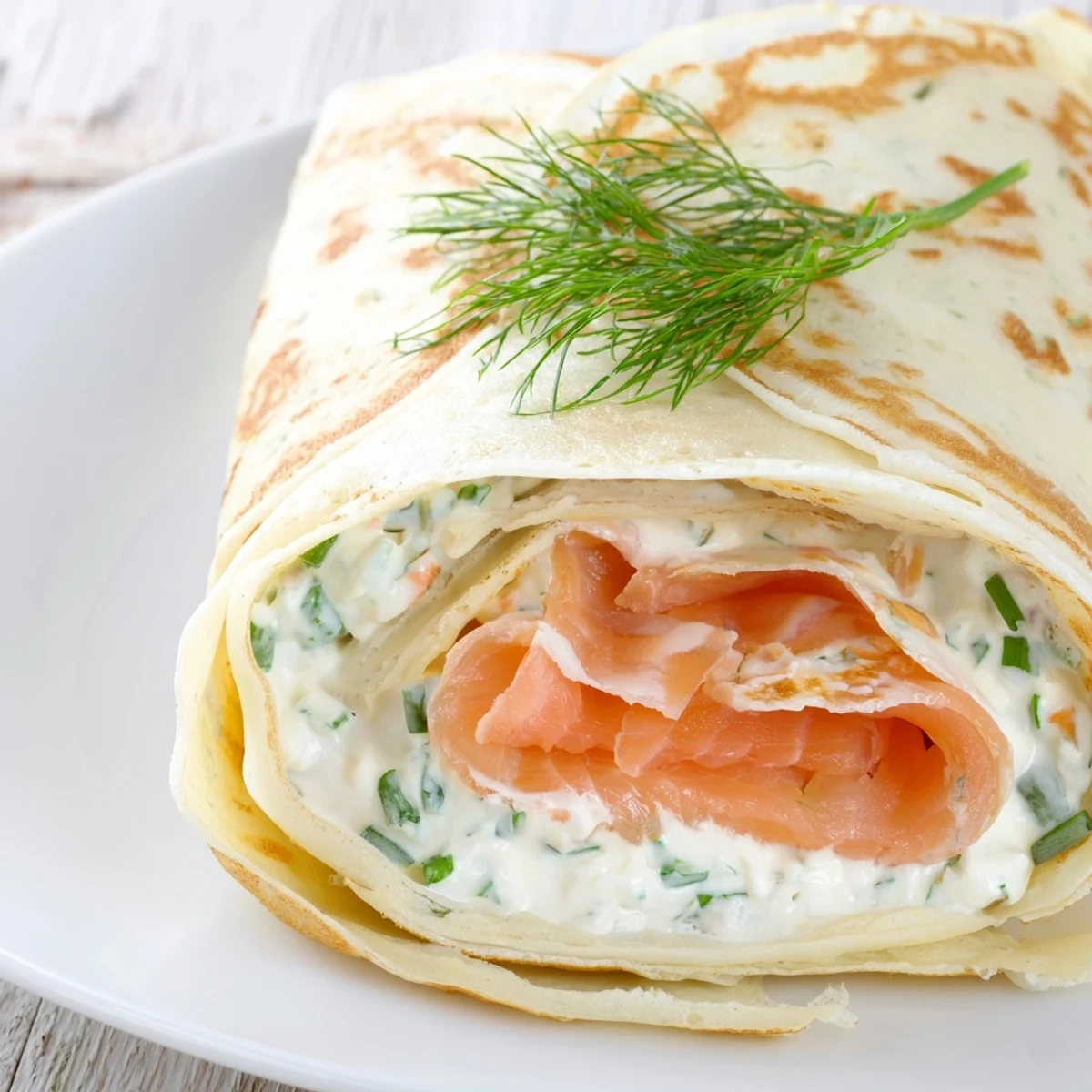 Golden rolled crepes filled with creamy herbed cheese and thinly sliced smoked salmon garnished with fresh dill.