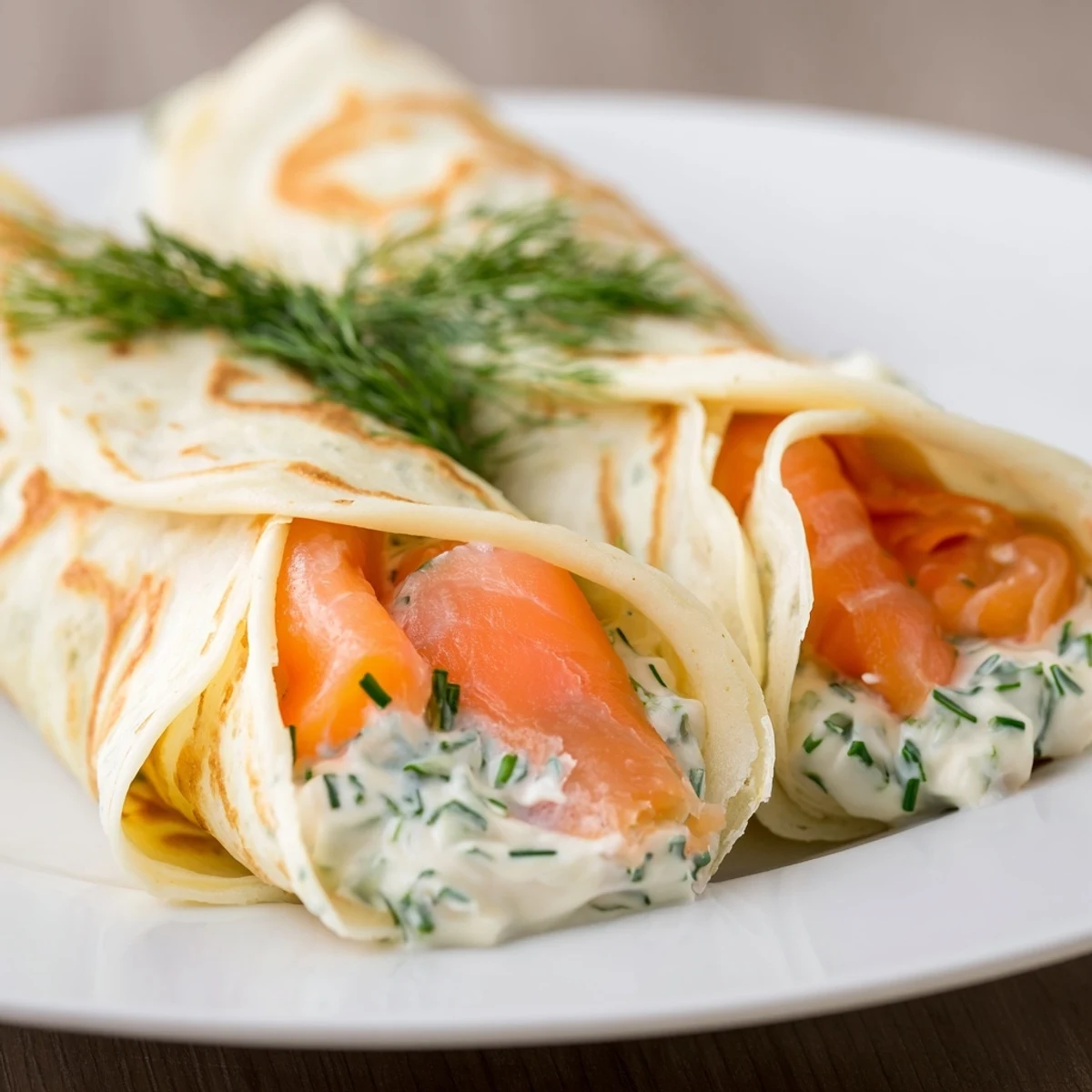 Elegant brunch dish featuring thin crepes rolled with smoked salmon and topped with lemon wedges and chives.