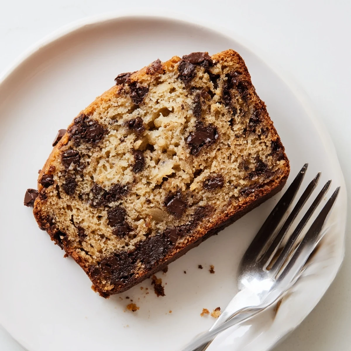 Golden chocolate chip banana bread loaf with melted chocolate pockets on a rustic wooden board