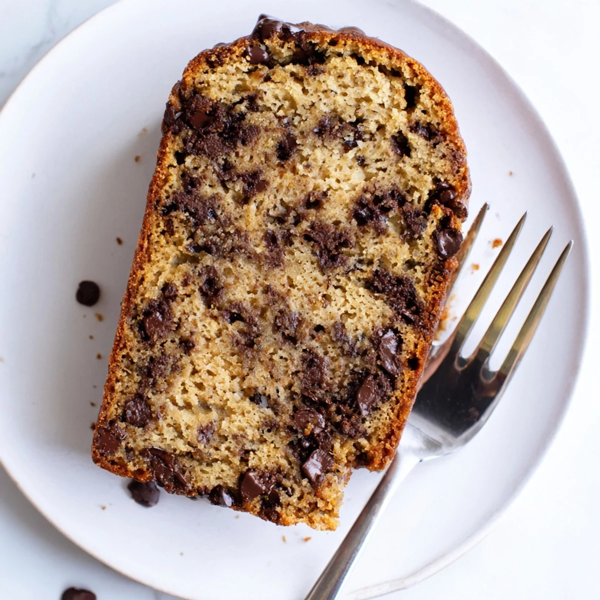 Slice of moist chocolate chip banana bread revealing dark chocolate morsels on a white plate