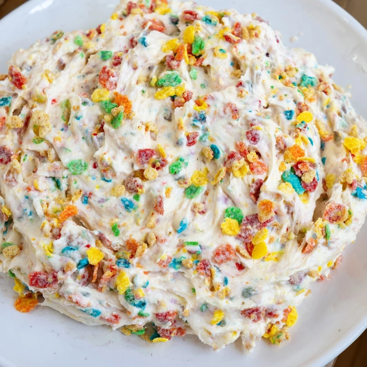 Vibrant bowl of homemade Fruity Pebbles frosting showing rainbow specks throughout the creamy white mixture