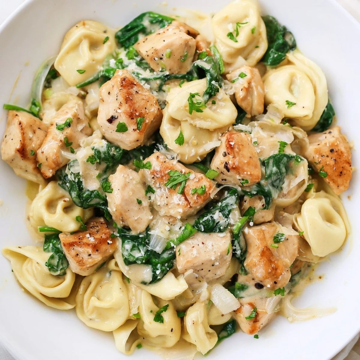 Steaming plate of creamy garlic chicken tortellini with spinach topped with Parmesan