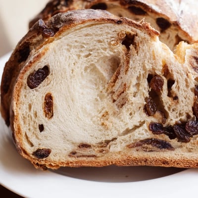A sliced rustic Cinnamon Raisin Artisan Bread reveals plump raisins and a soft, spiced crumb inside.  