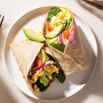 This High Protein Breakfast Wrap with Cottage Cheese and Avocado is cut in half to reveal its colorful layers of eggs, avocado, and crisp vegetables, resting on a clean kitchen counter with morning light.
