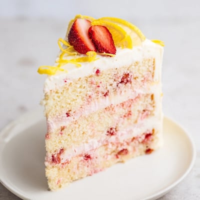 Moist Strawberry Lemonade Cake With Creamy Lemon Buttercream frosted and topped with lemon slices and berries.