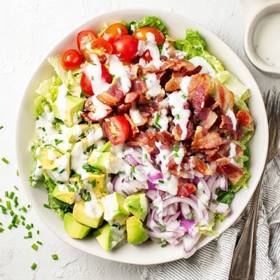 A bowl of Crispy Bacon Keto BLT Salad with avocado and red onion slices.